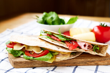Piadina Romagnola with mozzarella cheese, tomatoes, ham and rocket salad on a cutting board on the table. Italian flatbread or open sandwich. Selective focus.