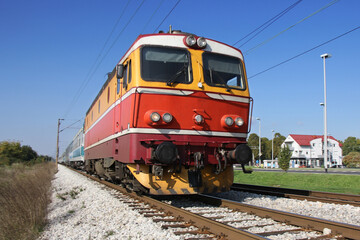 Obraz premium Red passenger train passing railroad on a sunny day