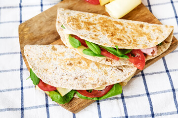 Piadina Romagnola with mozzarella cheese, tomatoes, ham and rocket salad on a cutting board. Italian flatbread or open sandwich. Selective focus.