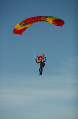 Skydiver under the canopy of a bright parachute is preparing for landing.