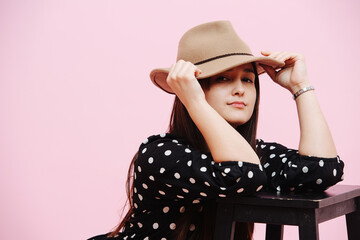 Portrait of a pretty, temperate young sitting woman leaning on a stool.