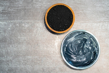 Charcoal, crushed fraction, homemade face mask and activated charcoal scrub of powder and yoghurt on white wooden background