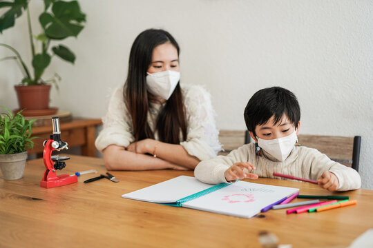 Asian Nanny Doing Home Works With Little Child While Wearing Safety Face Mask For Coronavirus Outbreak - Daycare Concept