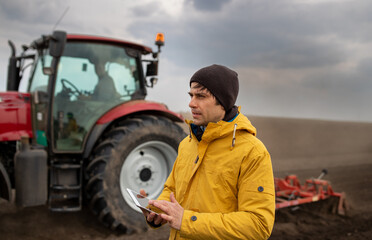 Farmer with tablet in front of tractor in field