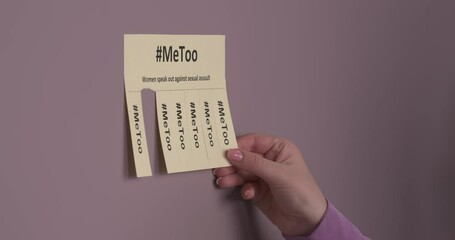 Unrecognizable women tearing off tabs from flyer pasted to a wall with Me Too hashtag inscription. Women speak out against sexual assault.