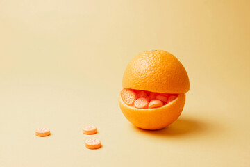 Orange stuffed with orange pills on yellow background. Vitamin C pills as an alternative to citrus...