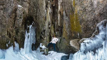 In the sheer granite rock, there is a narrow crevice in which a man stands. The leg is bent and touches the wall. The base of the cliff is icy covered with icicles. Baikal