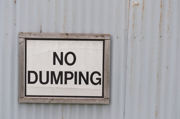 old NO DUMPING sign on a grey barrier