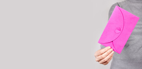 Hand with pink paper envelope on grey background.