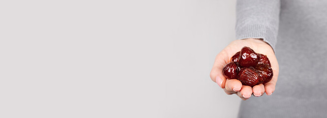 Hand with dried date on grey background.