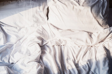 Crumpled bedding with pillow in the bedroom with sunlight in the morning
