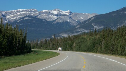 Fototapeta premium driving down a lonely road to the mountains with a forest on each side