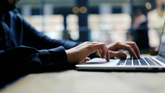man touches the touchpad of a laptop at a table in a cafe