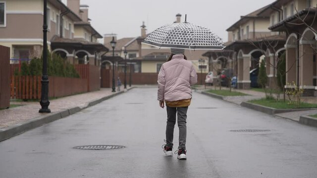 The girl walks down the street in the rain with an umbrella. A beautiful quarter of a myth with small houses in the English style on the street yagoko goes teenager with an umbrella. Slow motion 4K vi