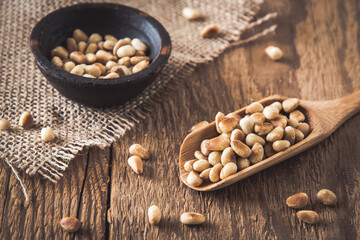 Pine nuts on a wooden spoon and in a small bowl on a wooden background