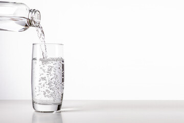 Wasser aus einer Flasche im Glas wird eingeschenkt vor weißen Hintergrund