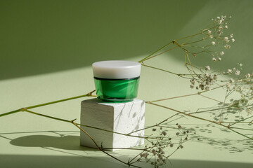 Product concept beauty, body care. White 3D podium, jar For cream , sprig of flowers on green pastel background. Hard shadows from the sunlight, copy space