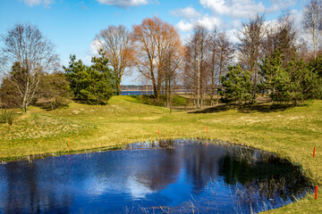 Sunny spring landscape with small lakes on flooded meadows on the banks of Kisezers in Riga, Latvia. White cumulus clouds are reflected in the water.