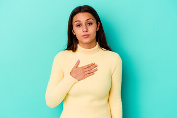 Young Indian woman isolated on blue background taking an oath, putting hand on chest.