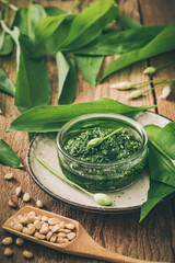 Homemade wild garlic pesto in a glass bowl on wooden background, decorated with leaves and pine...