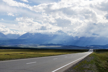 The road in the high-mountainous steppe. Mountains and cloudy sky.