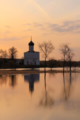 Fototapeta na wymiar Watercolor dawn landscape in high water - with the silhouette of a church and reflections on the surface of a meadow flooded with melting snow.