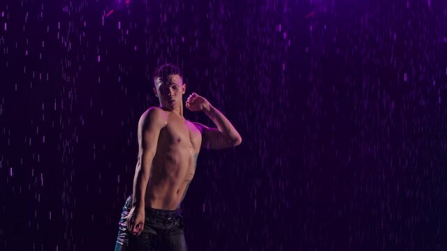Contemporary ballet, man performs elements of modern choreography, standing on surface water in rain. Sensual movements of male dancer with naked torso. Silhouette. Close up. Slow motion.
