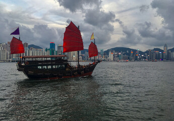 Traditional Chinese junk with red sails in Victoria Harbor, Hong Kong in China with panoramic city...