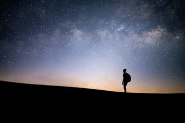 Silhouette of young traveler and backpacker watched the beautiful night sky, star and milky way alone on top of the mountain. He enjoyed traveling and was successful when he reached the summit.