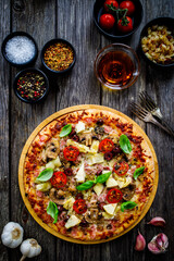 Pizza capricciosa with white mushrooms, ham, artichoke, tomatoes, olives, parmesan and mozzarella on wooden background

