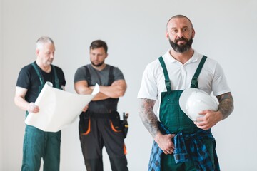 Crew of three professional builder wearing overalls standing in empty interior