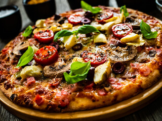 Pizza capricciosa with white mushrooms, ham, artichoke, tomatoes, olives, parmesan and mozzarella on wooden background
