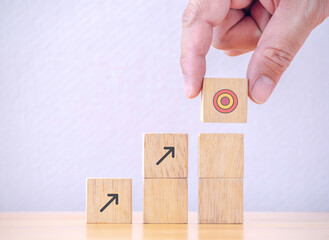 Businessman putting to arranging wood cube with arrow stacking step stair to objective target. Business achievement goal and growth success objective concept.