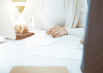 Accountant checking financial statement or counting by calculator income for tax form, hands closeup. Business woman sitting and working with colleague at the desk in office. Tax and Audit concept