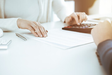 Accountant checking financial statement or counting by calculator income for tax form, hands closeup. Business woman sitting and working with colleague at the desk in office. Tax and Audit concept