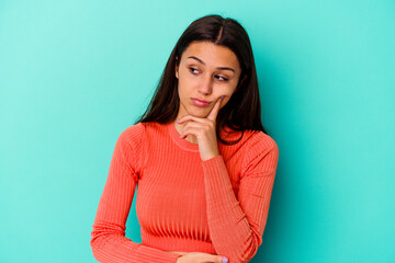 Young Indian woman isolated on blue background contemplating, planning a strategy, thinking about...