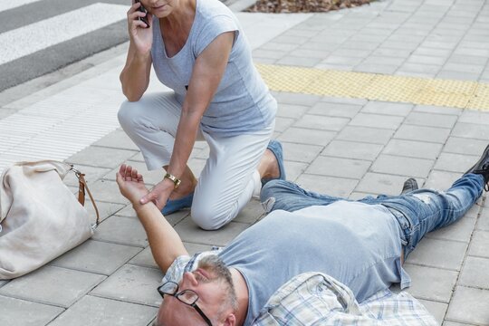 Senior Passerby Kneels Beside The Person Who Fainted On The Street And Calls An Ambulance