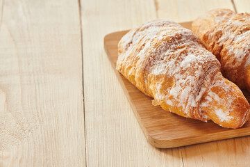 Tasty croissants with powdered sugar on wooden board. Traditional french pastry on the breakfast. Close up view with copy space.