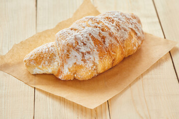 Tasty croissants with powdered sugar on wooden board. Traditional french pastry on the breakfast. Close up view