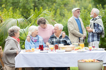 Cheerful group of elderly friends during barbeque at garden of family home