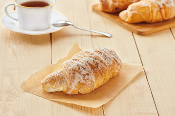 Tasty croissants with powdered sugar for the breakfast on wooden board. Traditional french pastry on the breakfast. Close up view