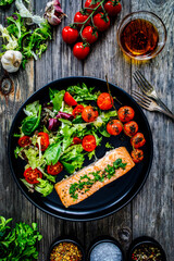 Roasted salmon steak with roast potatoes and vegetable salad served on black plate on wooden table
