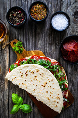 Italian piada wraps - piadina stuffed with fresh vegetable leaves and salami sausage on wooden table
