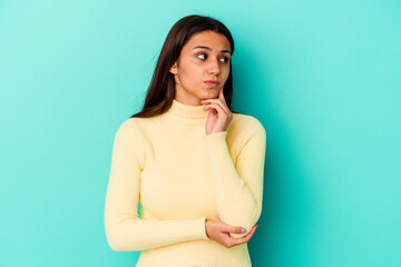 Young Indian woman isolated on blue background thinking and looking up, being reflective, contemplating, having a fantasy.