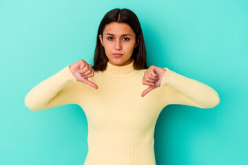 Young Indian woman isolated on blue background showing a dislike gesture, thumbs down. Disagreement...