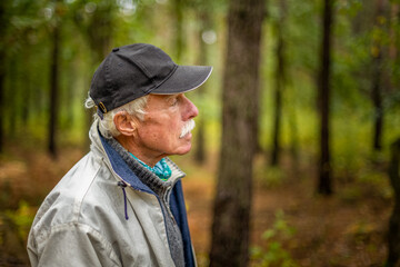A mature man wearing a cap walking in the woods during the day.