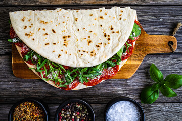 Italian piada wraps - piadina stuffed with fresh vegetable leaves and salami sausage on wooden table

