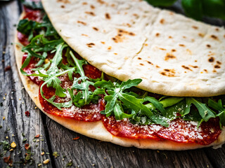 Italian piada wraps - piadina stuffed with fresh vegetable leaves and salami sausage on wooden table
