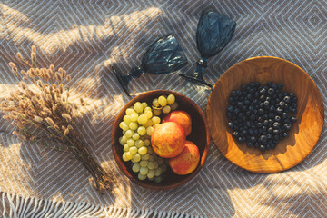 Summer picnic. Fresh  fruits in wooden plates and wineglasses on  blanket in sunny light in meadow
