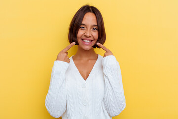 Young mixed race woman isolated on yellow background smiles, pointing fingers at mouth.